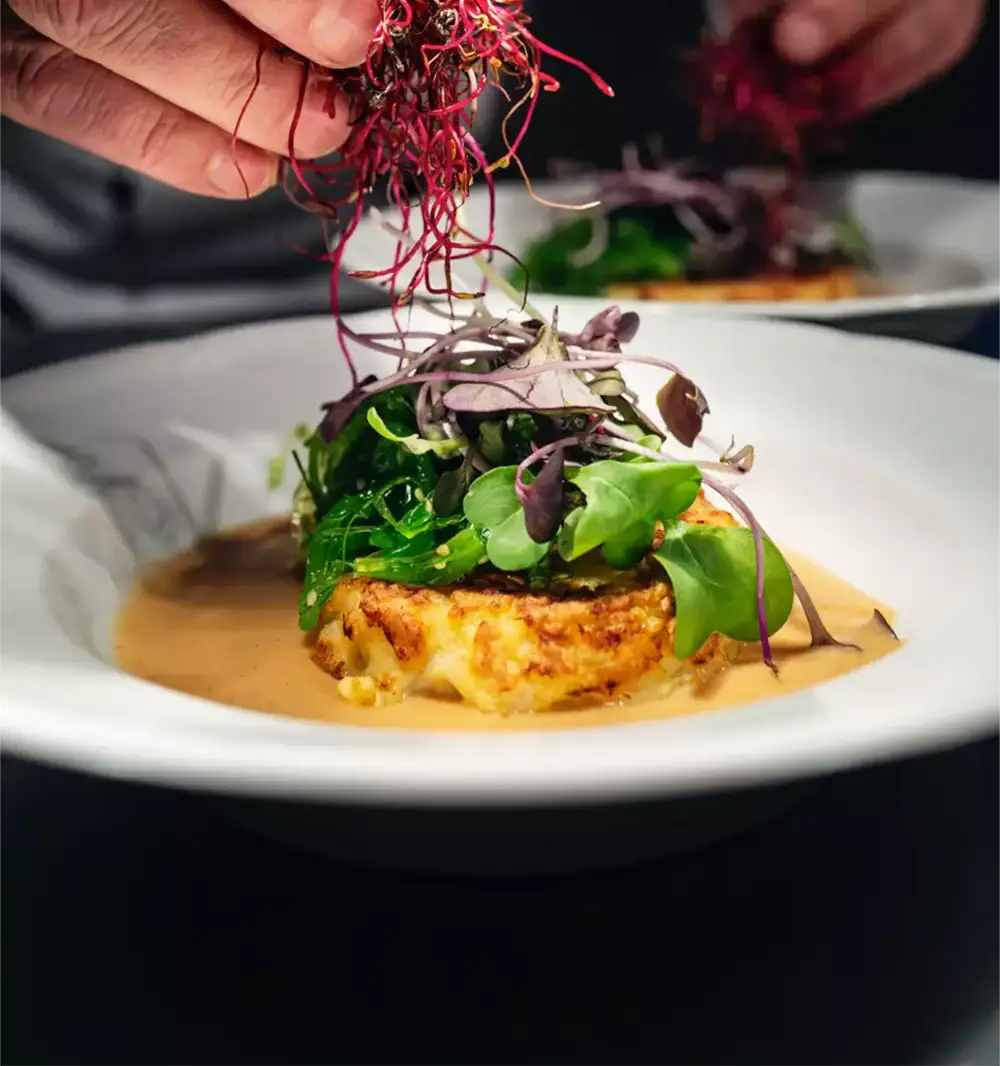 Chef garnishing a plated entrée with fresh microgreens